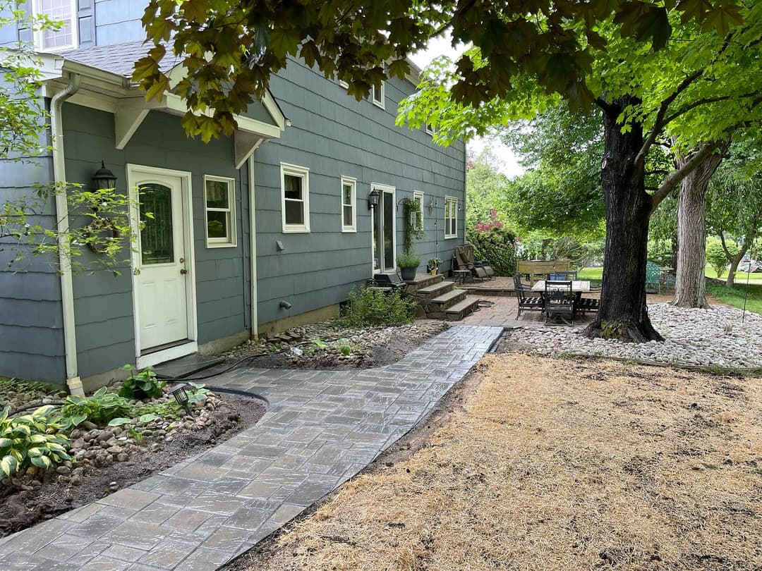 Modern home exterior with a paved walkway, garden landscaping, and outdoor seating area.