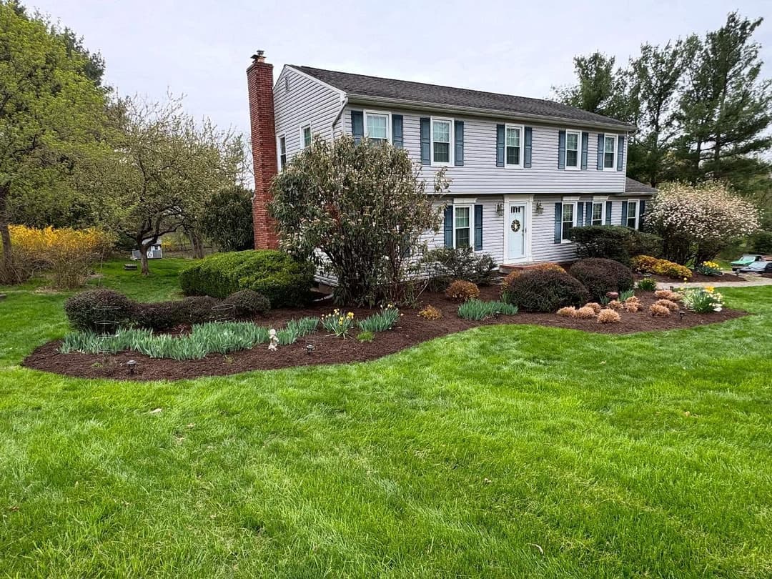Two-story home with landscaped garden featuring shrubs and colorful flowers in a green yard.