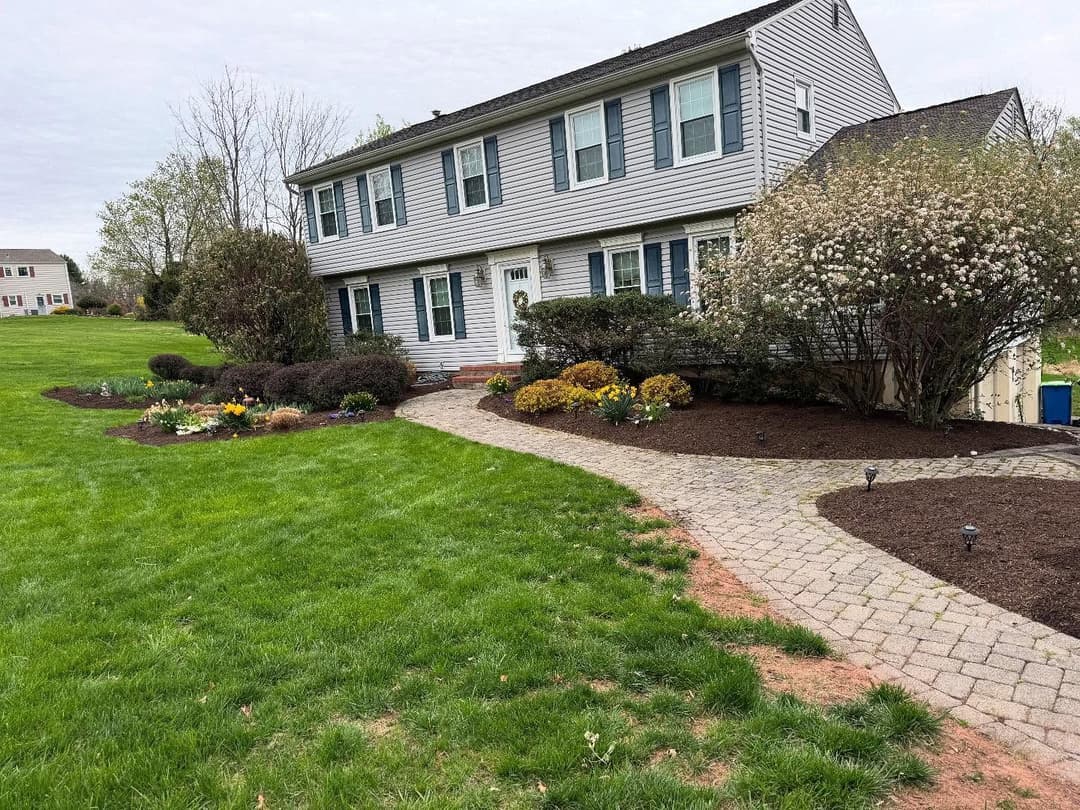 Two-story suburban house with landscaped garden and stone pathway in a green yard.