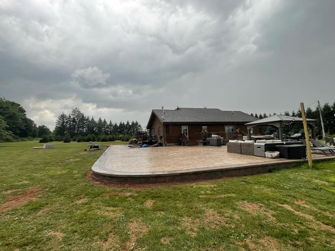 Spacious backyard with a patio and log cabin under a cloudy sky, surrounded by greenery.
