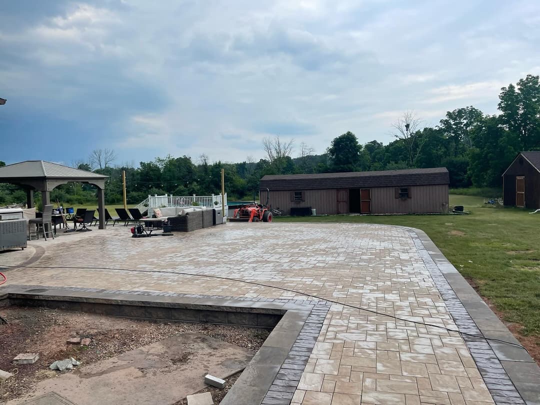 Paved patio area with outdoor furniture, shed, and green landscape under a cloudy sky.