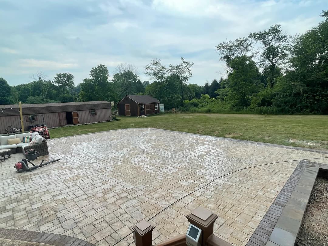 Largely paved outdoor area with stone finish, surrounded by green trees and structures.