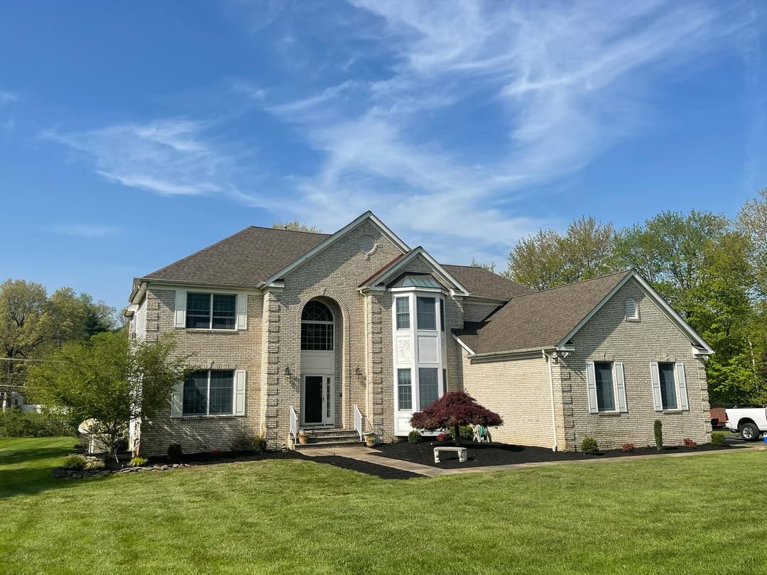 Two-story brick house with a manicured lawn, modern architecture, and bright blue sky.