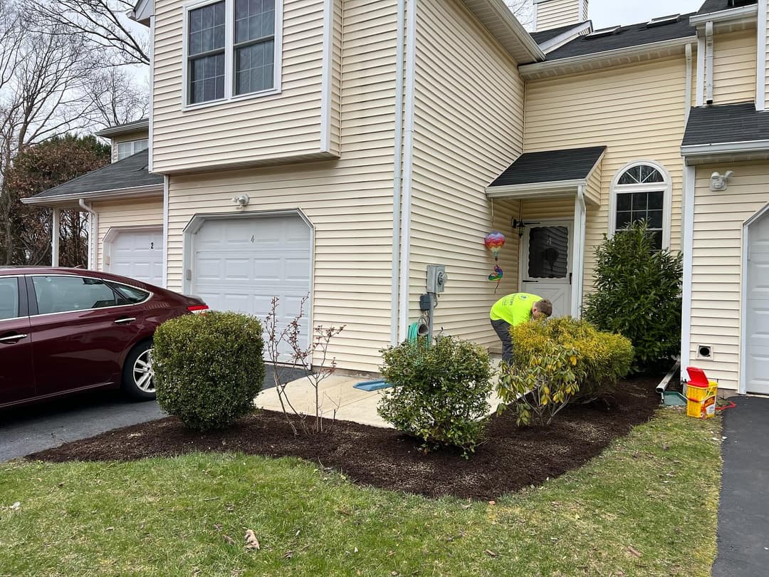 Landscaper planting shrubs near a home entrance, with a car parked in the driveway.