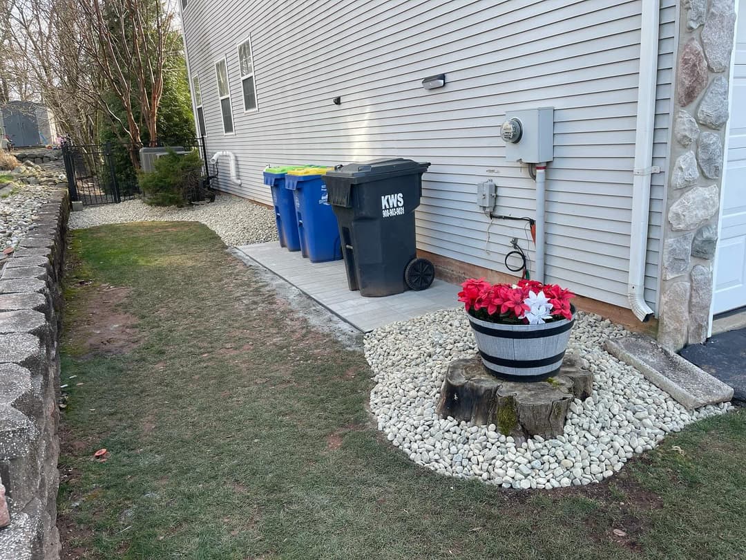 Side yard featuring garbage bins, a flower pot, and decorative gravel landscaping.