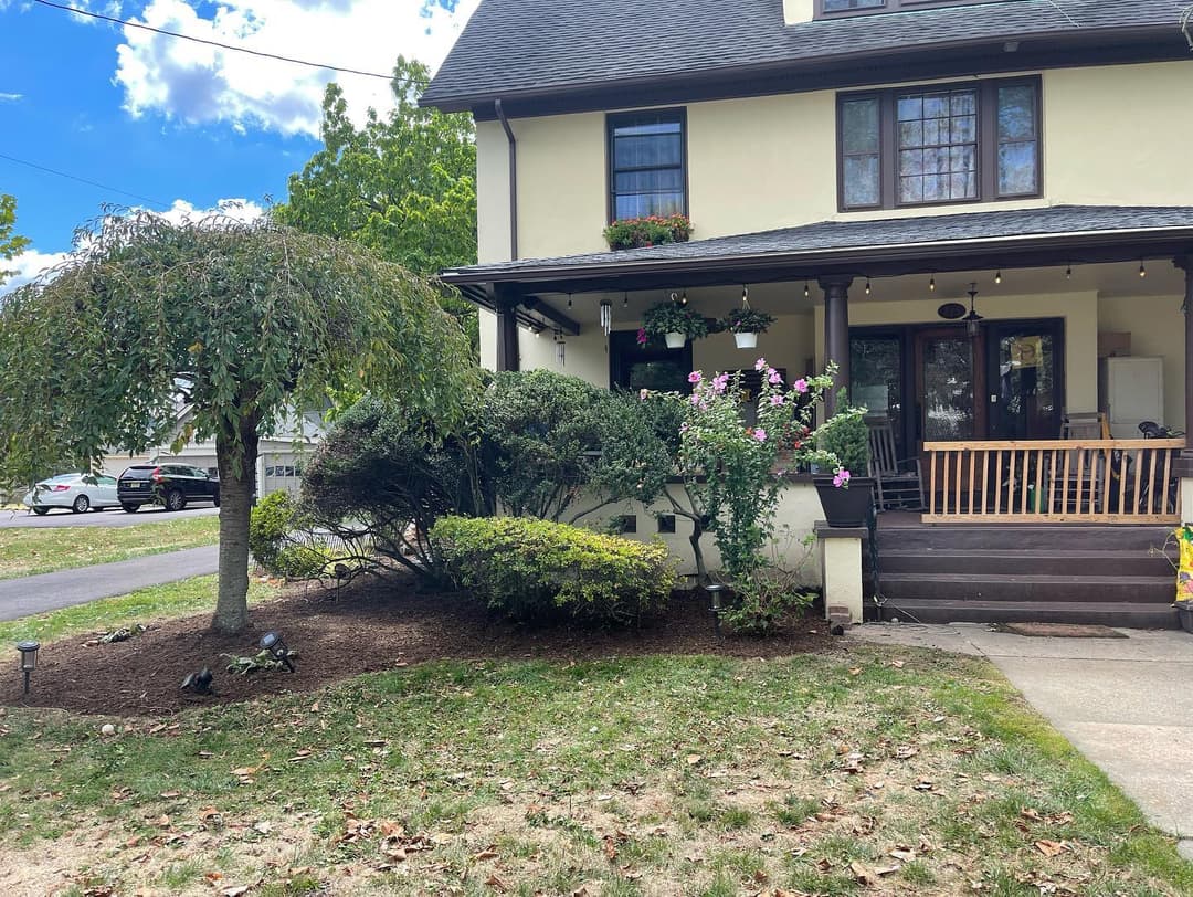 Victorian house exterior with manicured garden, flowers, and porch on sunny day.