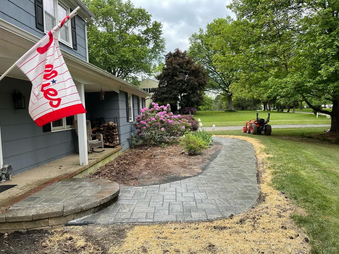 Front yard with a curved stone walkway, surrounded by greenery and a Chick-fil-A flag.