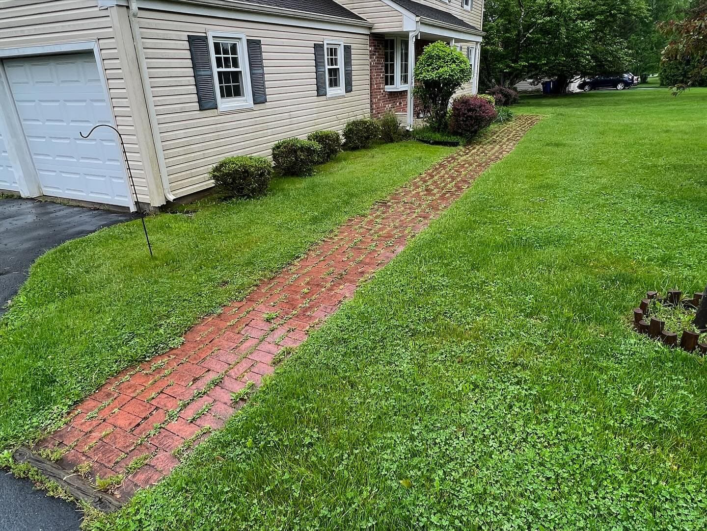 Brick walkway leading through lush green lawn to a suburban home.
